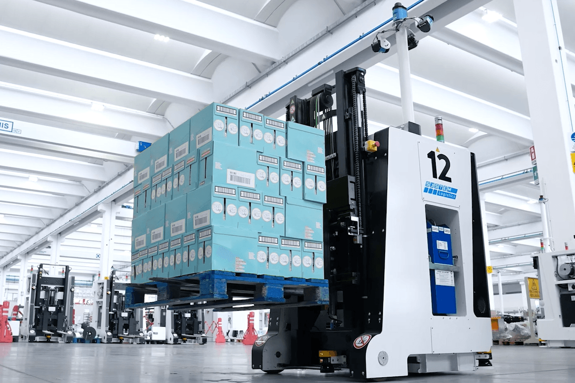 Ein automatisierter Gabelstapler transportiert eine Palette mit blauen Kartons durch ein gut beleuchtetes, poliertes Logistiklager mit weißen Trägern und sorgt so für einen effizienten Warenfluss.