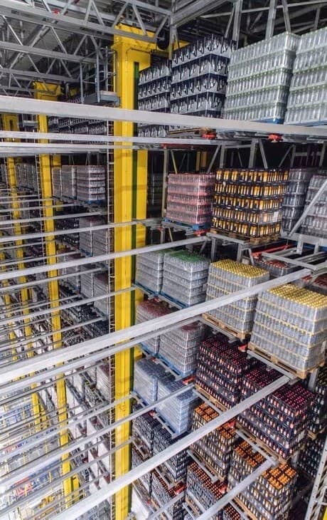 Hohe Lagerregale, beladen mit Paletten voller Getränke in Dosen und Flaschen, die in einem industriellen Logistikzentrum für einen effizienten Vertrieb angeordnet sind.
