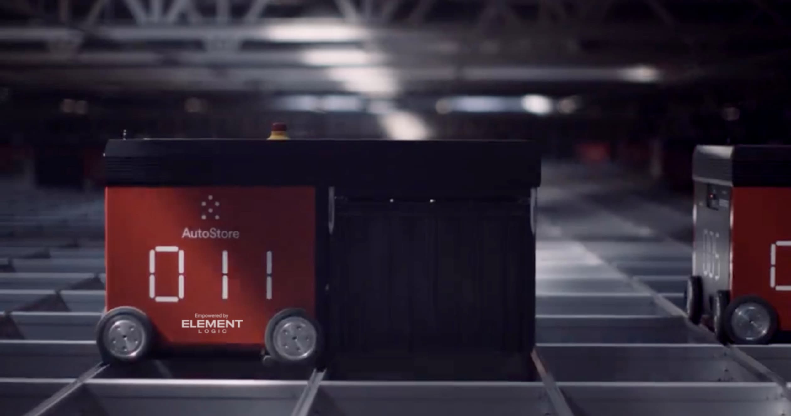 AutoStore-Roboter mit Nummer 011 und Element Logic Logo fährt auf dem Gitternetz eines automatisierten Lagersystems.