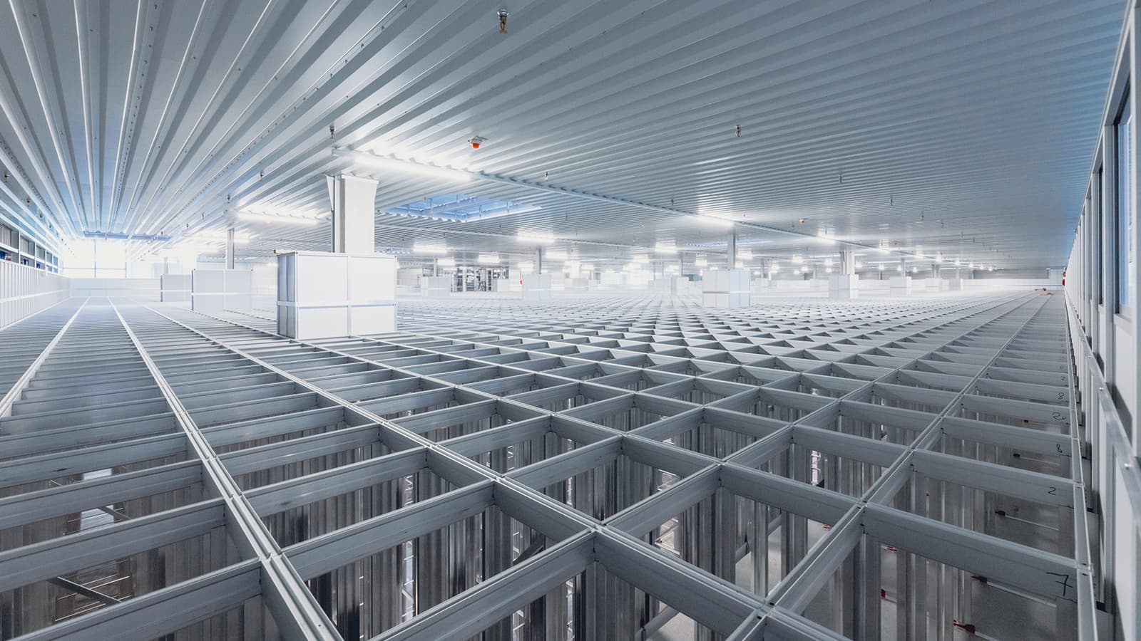 Interior of a large, modern warehouse featuring a grid-like structure with high ceilings and bright, uniform lighting. The grid consists of steel beams and columns, suggesting an automated storage or distribution system.