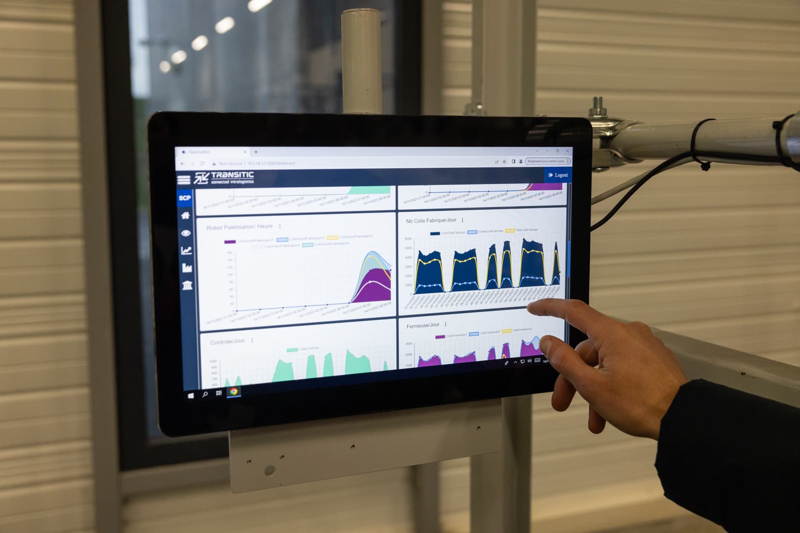 A person interacts with a touchscreen displaying data graphs and charts. The screen shows different visualizations, likely related to performance metrics. The setting appears to be an industrial or technical environment.
